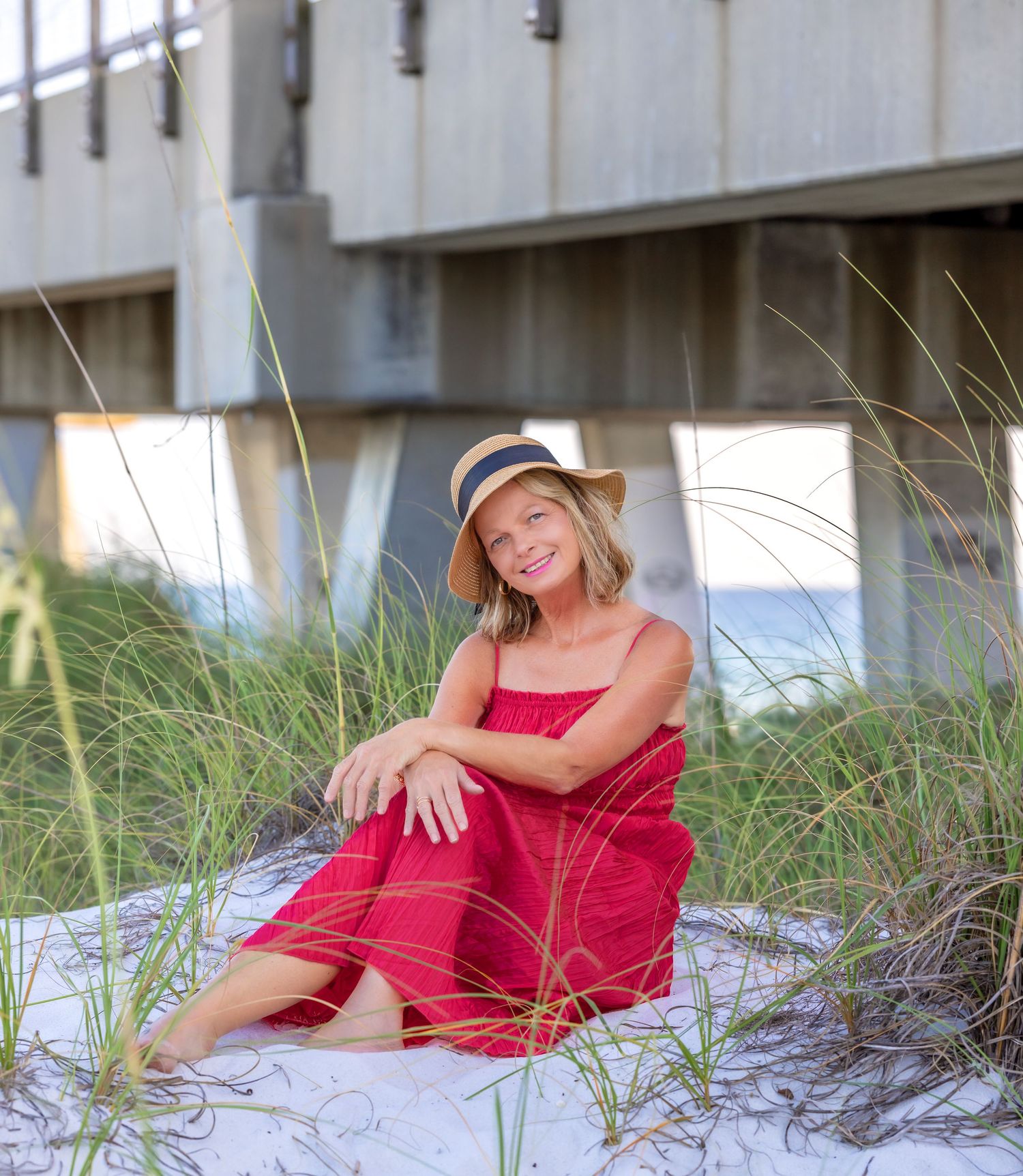 A person in a red dress relaxes on white sand dunes during a beachside photo session near the sea.