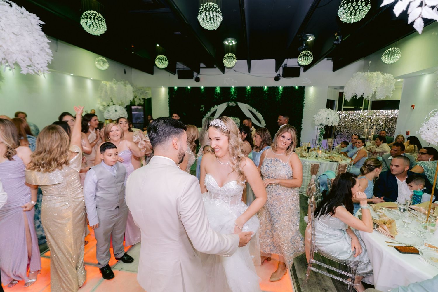 Wedding reception party guests dancing and enjoying themselves on a dimly lit dance floor under green spotlights.