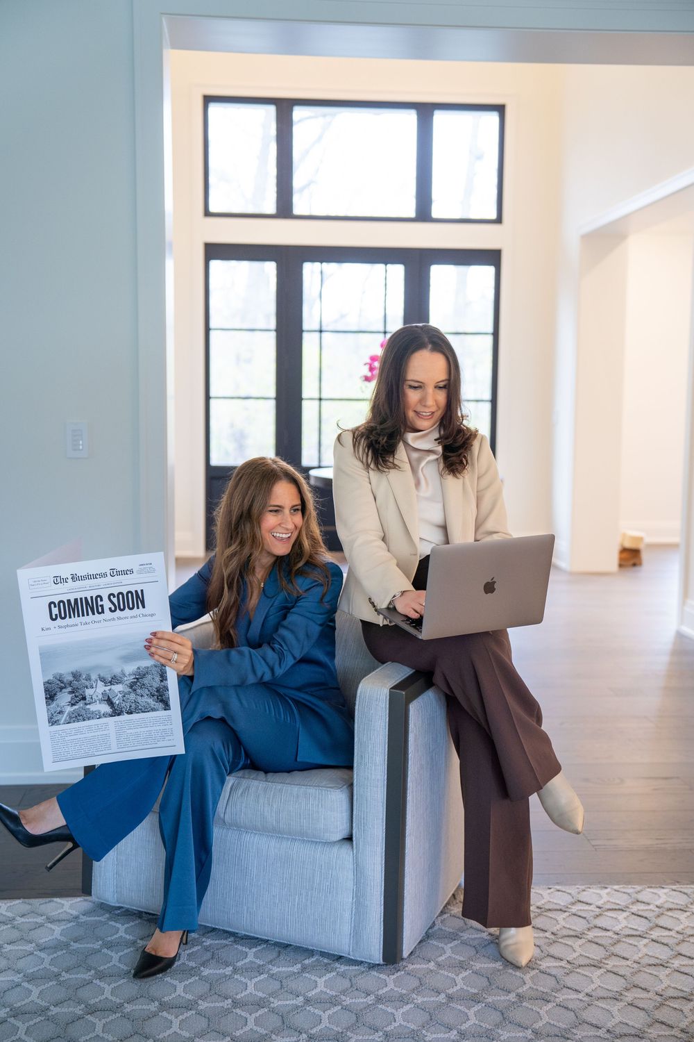 Two colleagues share a laugh while working together on a laptop in a bright modern office space.