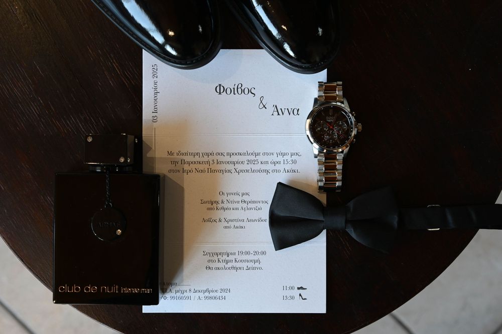Wedding invitation card with black bow tie and vintage watch on dark wooden surface.