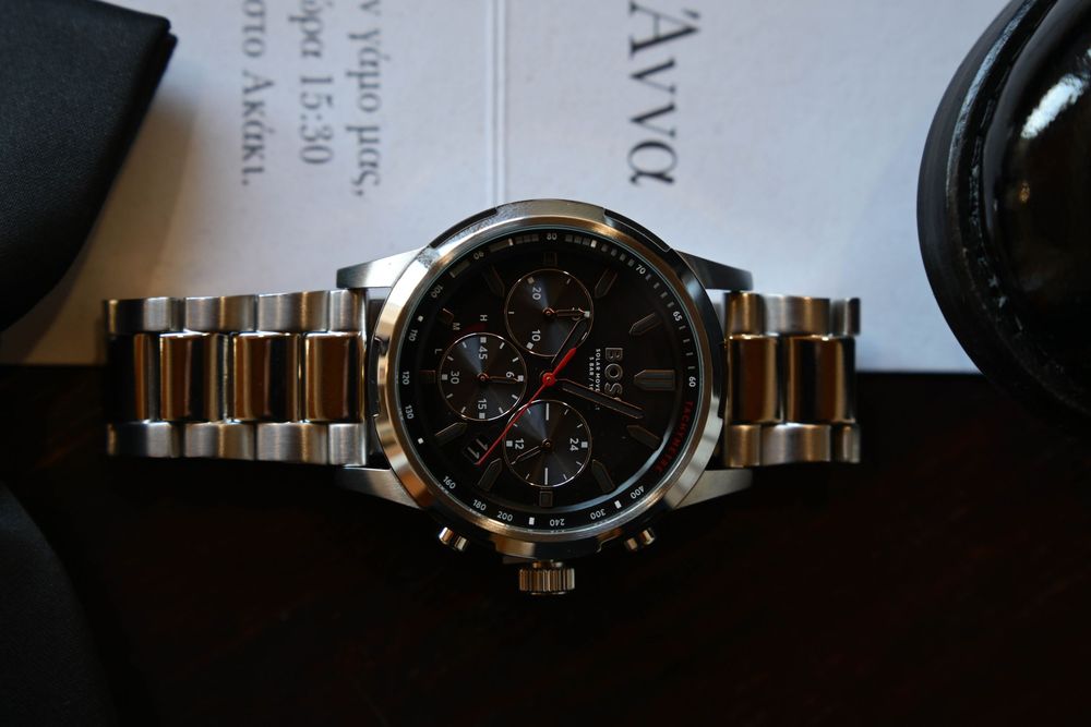 A luxury chronograph watch with silver metal band and black dial displayed on a dark surface.