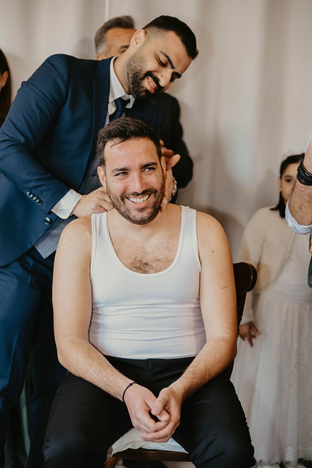 Several images show a man wearing a white tank top laughing and smiling while getting ready before a formal event.