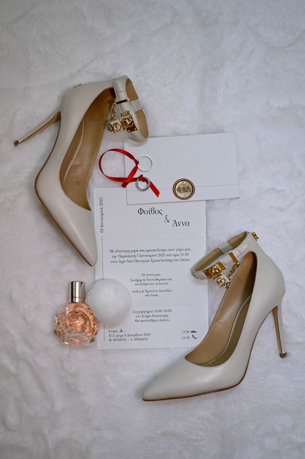 Wedding accessories flatlay with elegant white stiletto heels, perfume bottle, and invitation card on light fabric background.