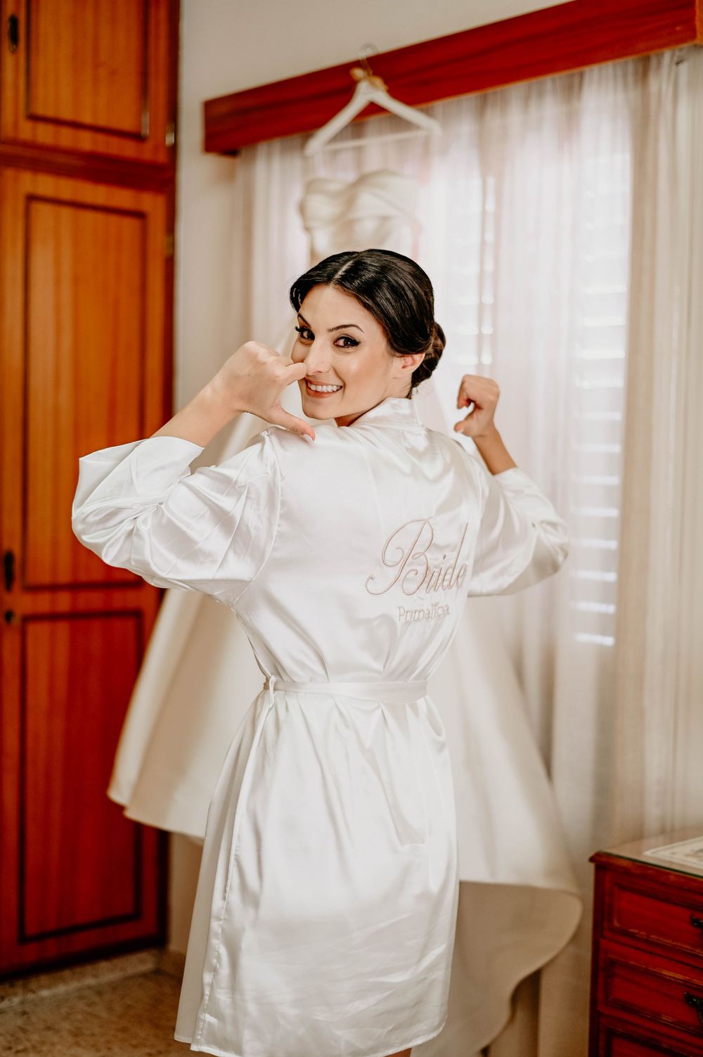 A person in a white silk robe getting ready in a wooden-paneled room with soft natural lighting through sheer curtains.