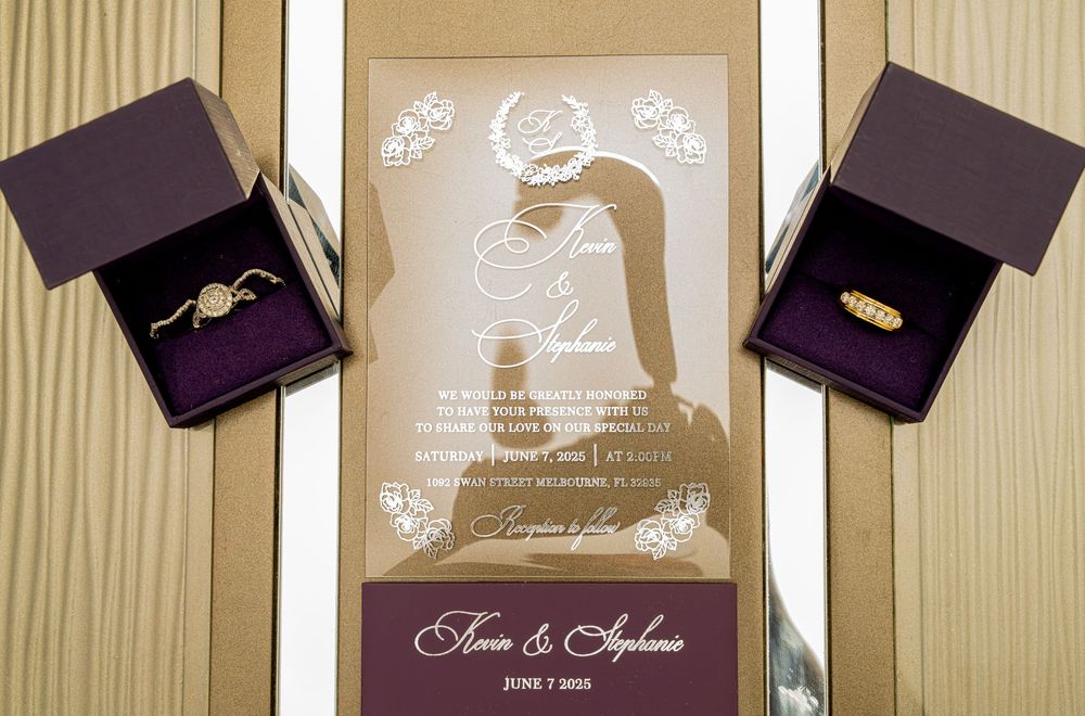 Elegant wedding invitation with gold artwork displayed between two ring boxes.