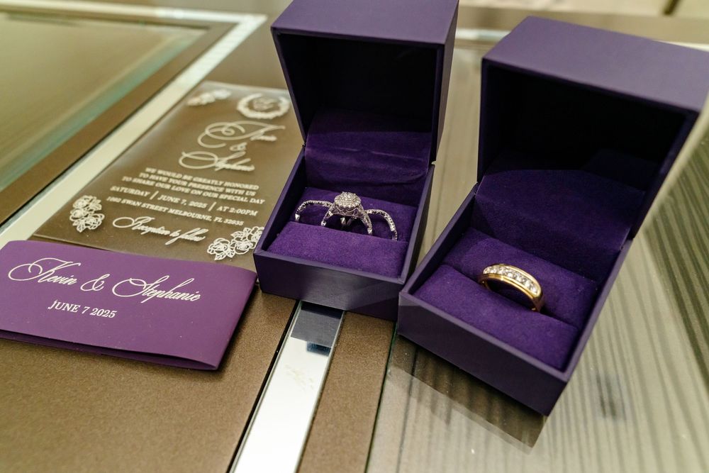 Wedding rings displayed in purple velvet boxes next to a formal invitation.