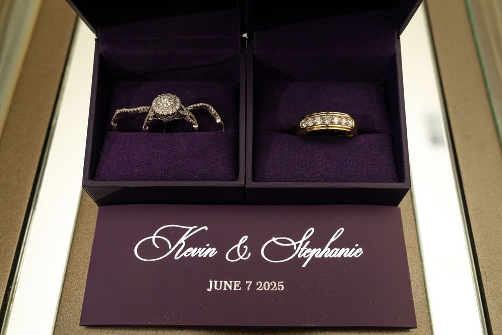 Wedding ring sets in purple boxes with couple's names and date displayed below.