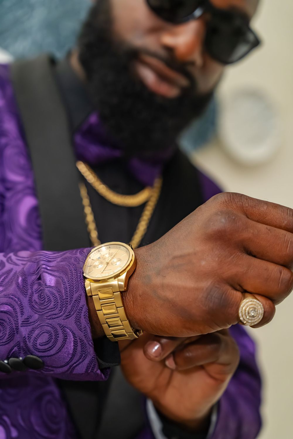 Close up of gold watch and jewelry accessories with purple suit sleeve.