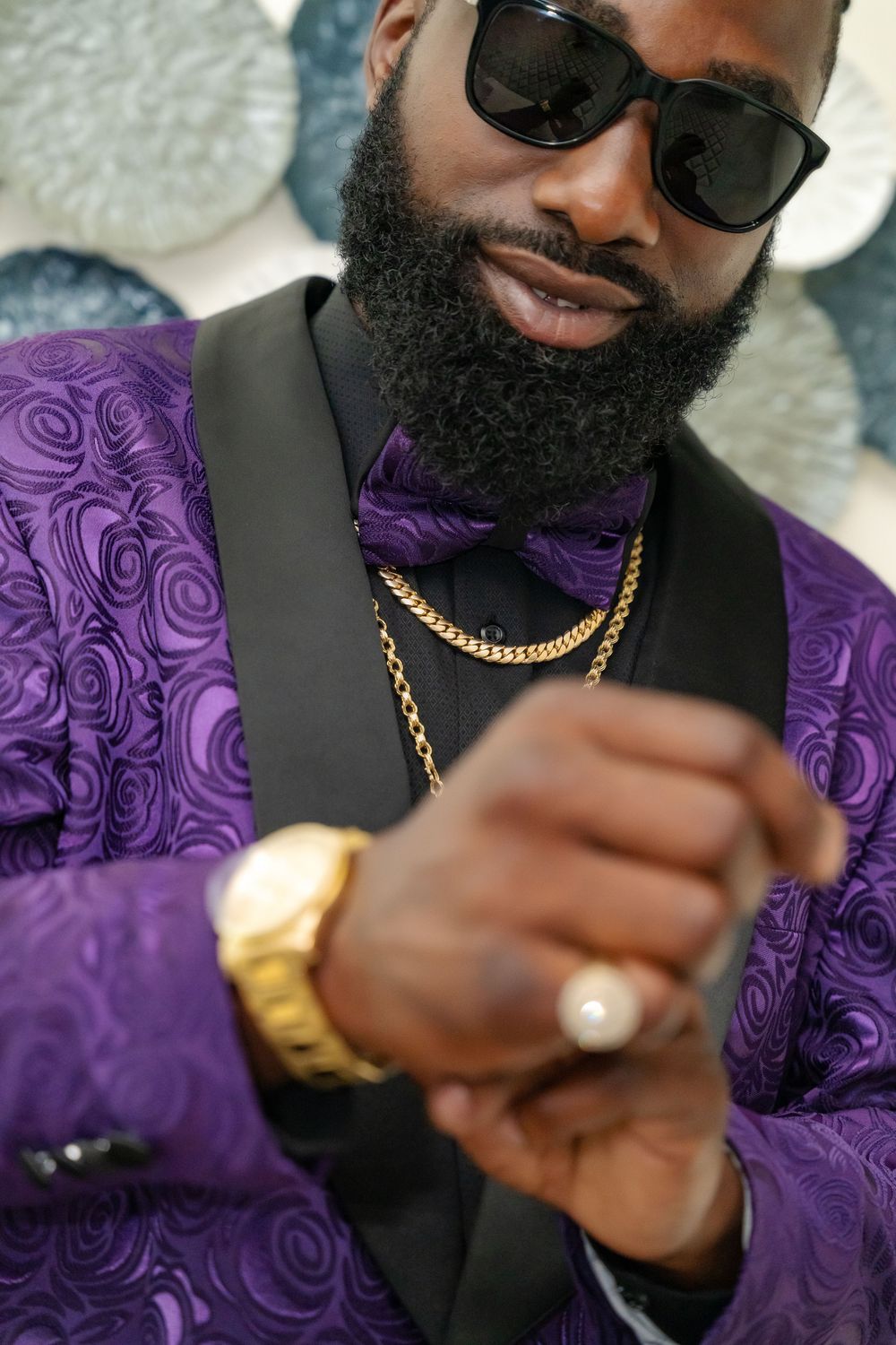 Detailed shot of gold chain necklace and accessories with purple paisley suit.