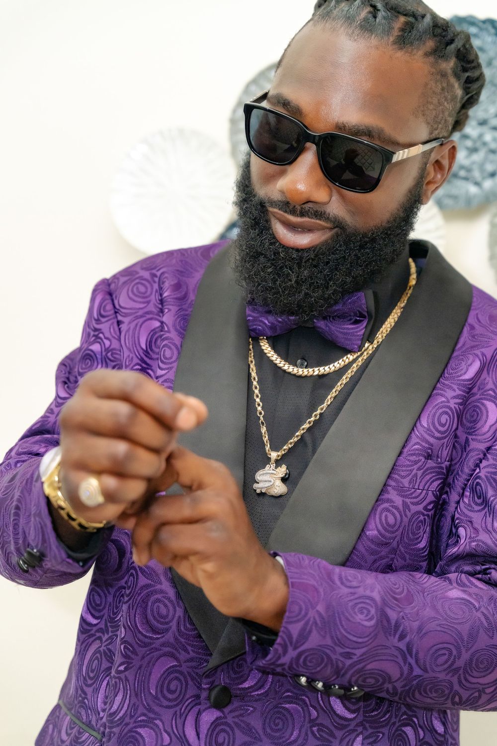 Close up showing braided hair, sunglasses and purple bow tie with gold pendant necklace.