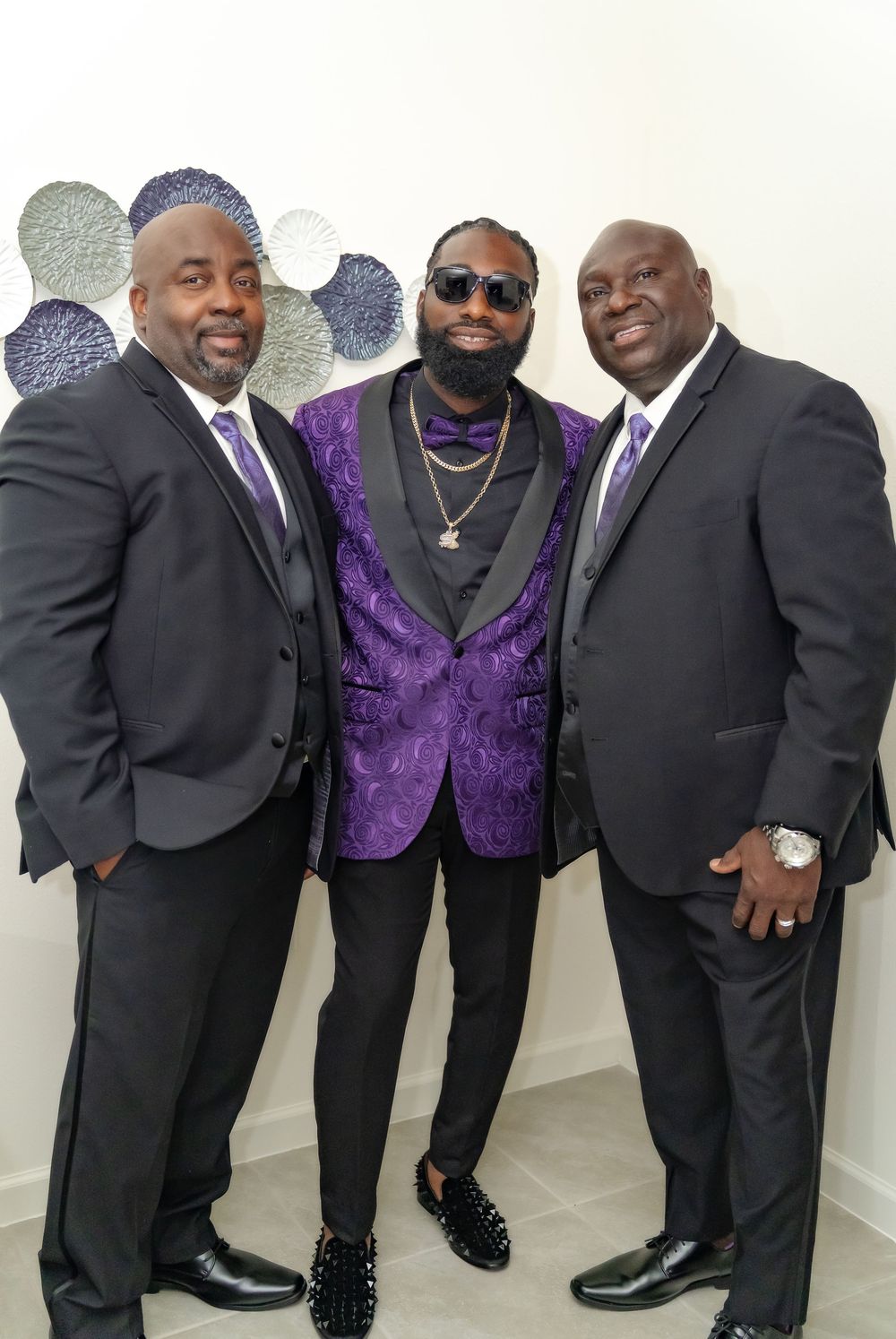 A group of men in formal attire with one wearing a distinctive purple patterned vest pose together.