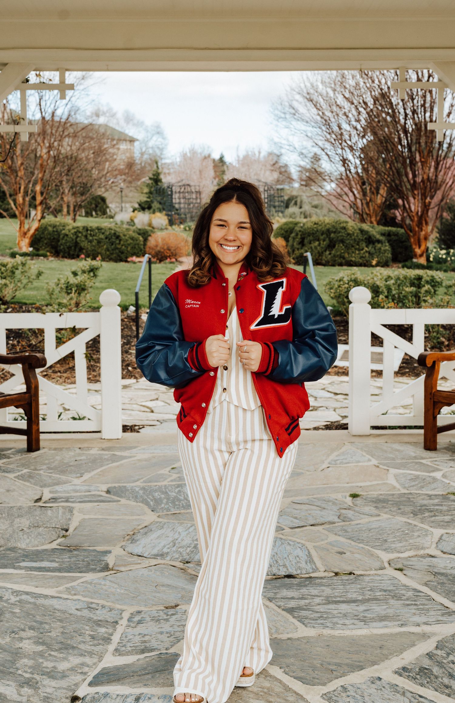 A high school senior in a red and blue varsity jacket posing for senior portrait photoshoot at Hershey Gardens.