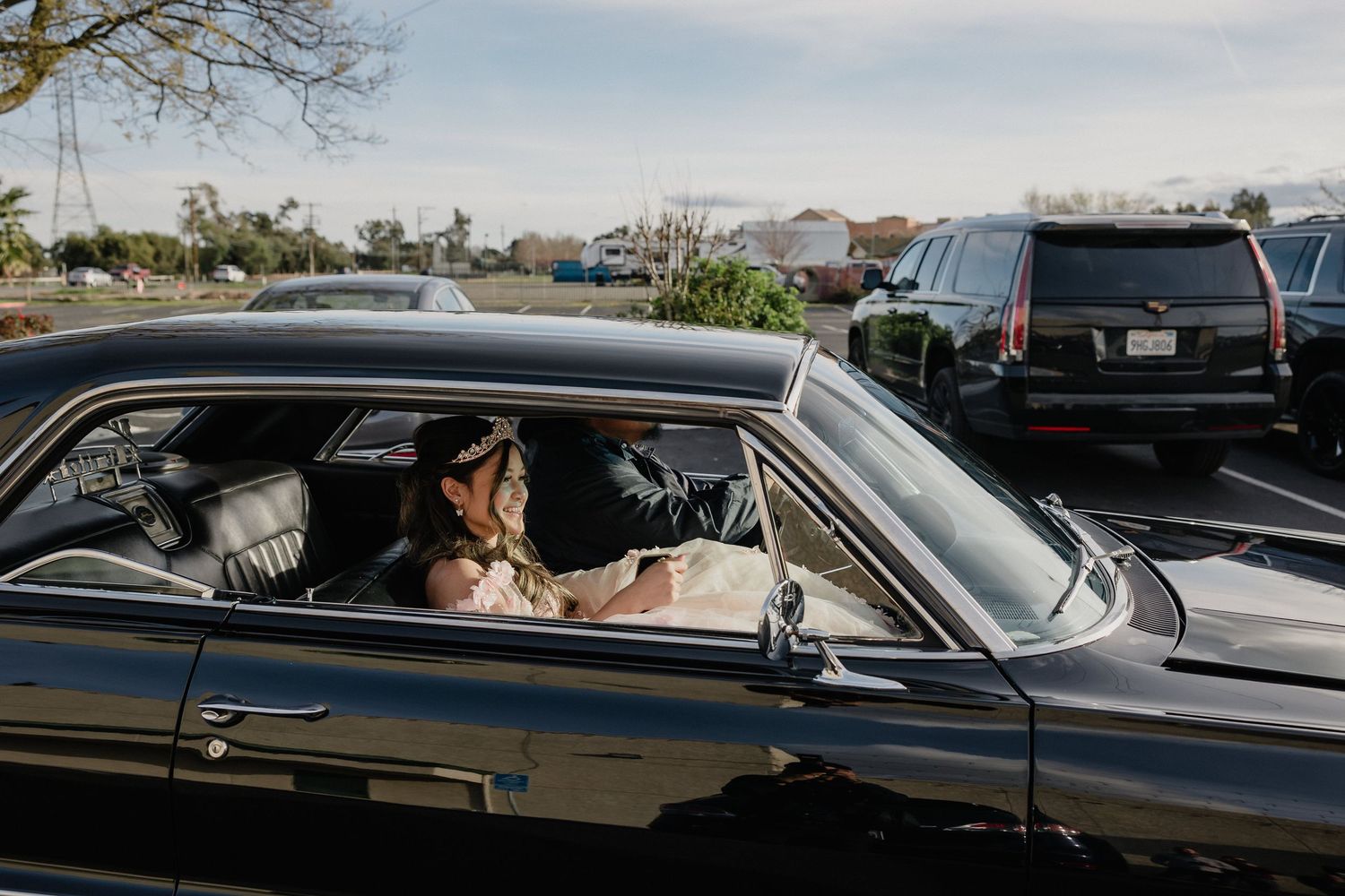 View through a car window of the quinceanera arriving to her venue, driven by a vintage black automobile.