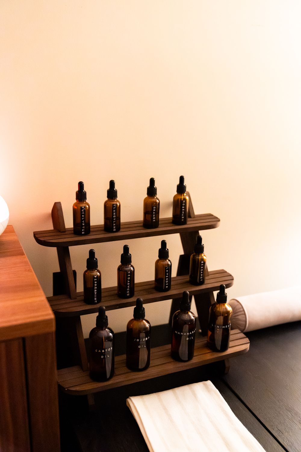Wooden display shelf holding dark glass essential oil bottles in rows.