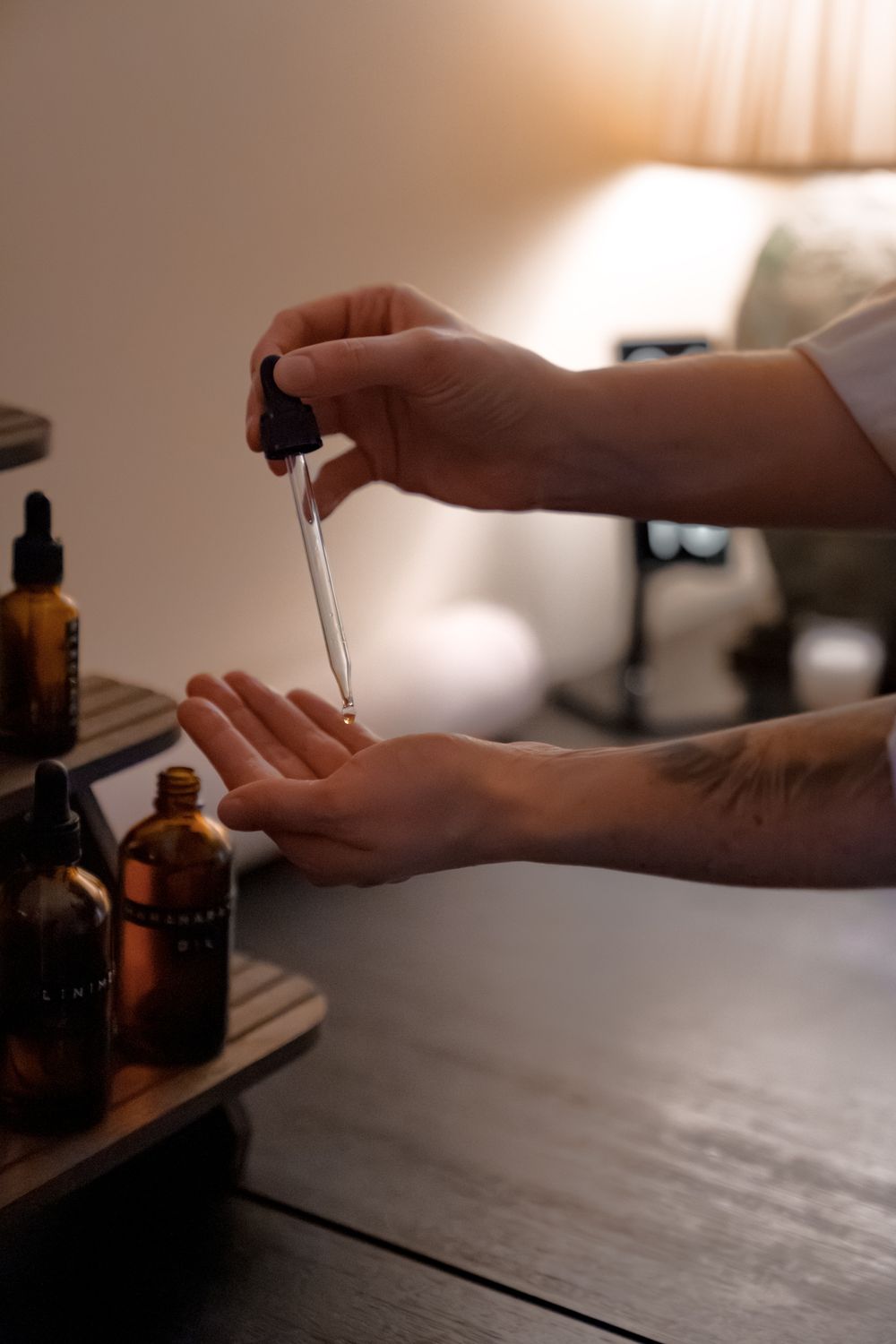 Hands using dropper bottle with amber essential oils on dark wooden surface.