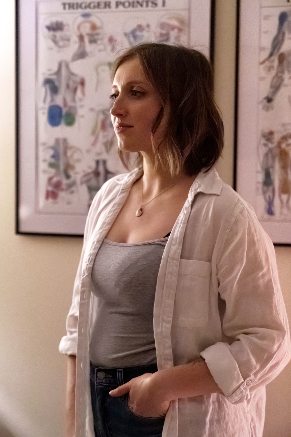 Healthcare professional in casual attire standing in office with anatomical charts on wall.