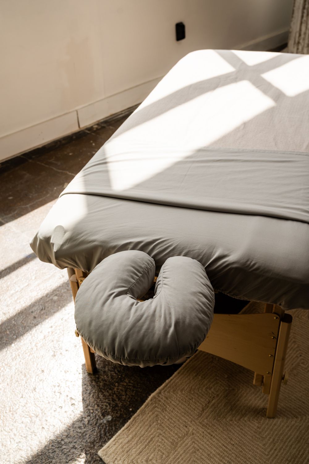 Massage table with gray cushion in sunlit room with natural lighting.