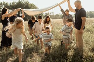 A joyful gathering of people playing in a sunlit field with a flowing fabric canopy overhead.