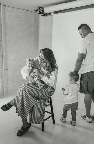 Black and white studio photo showing a family moment with parents and children in a minimalist white room setting.