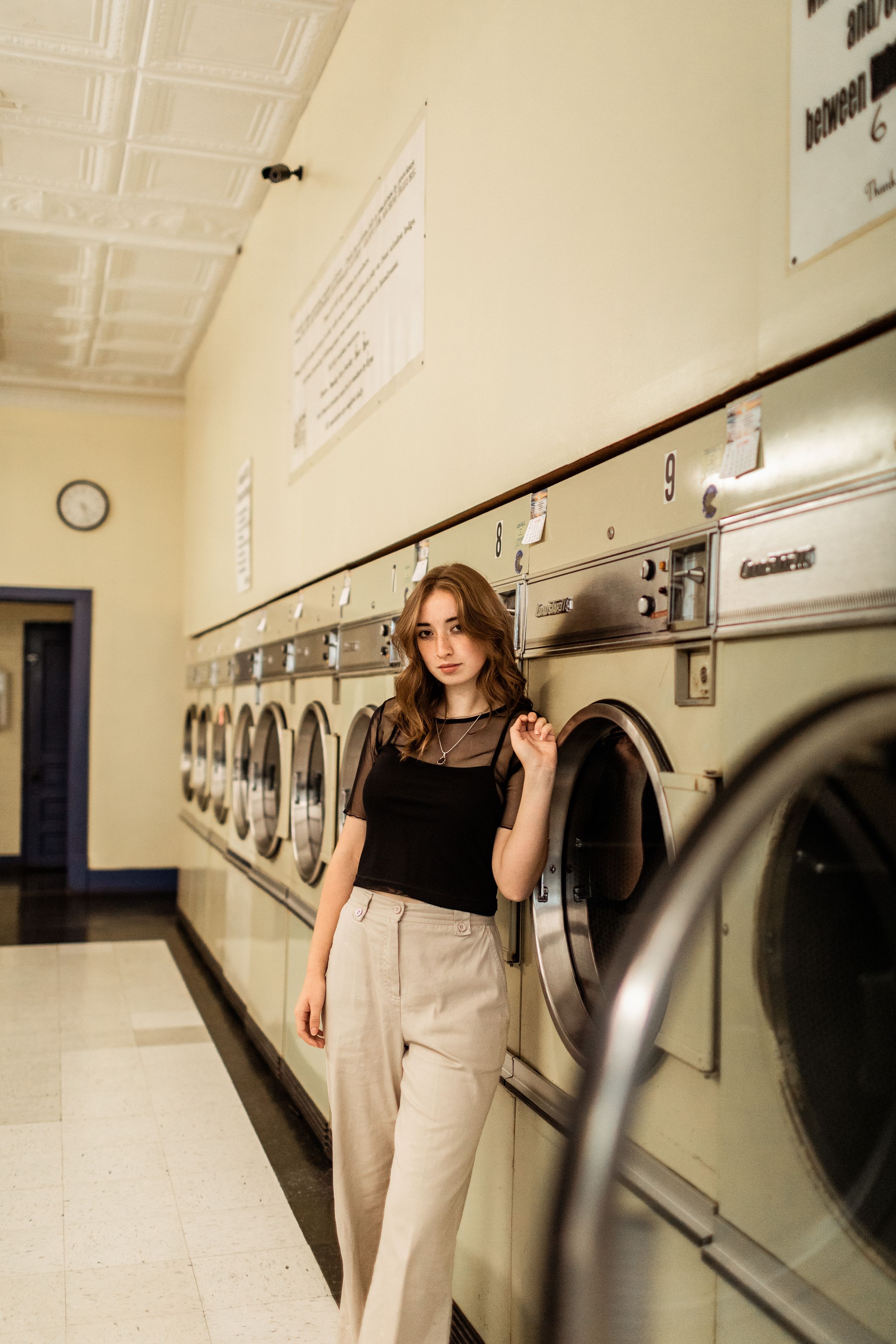 A stylish woman in black and beige standing in front of vintage washing machines at a laundromat.