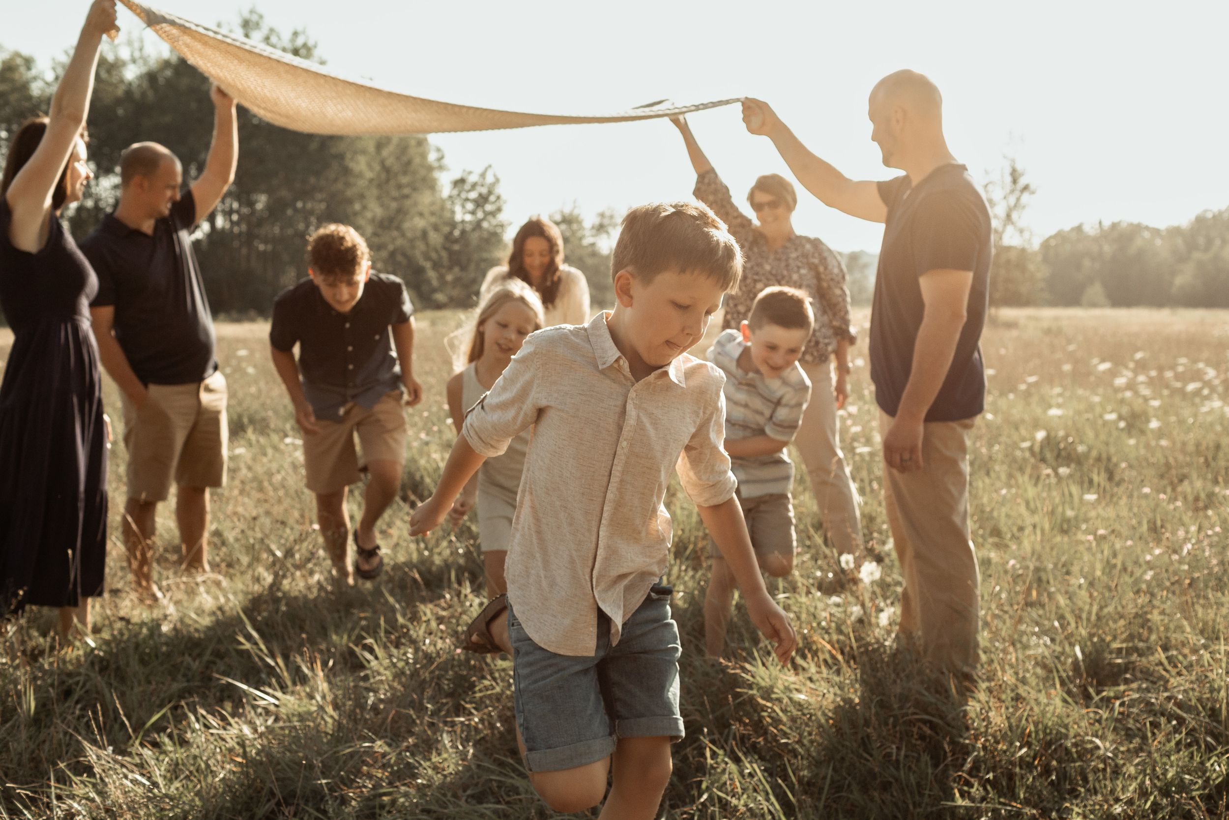 Group celebrates outdoors with fabric canopy during golden hour in summer field.
