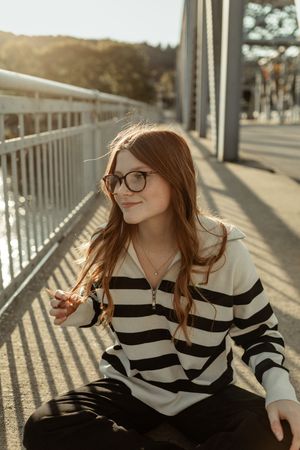 A person wearing glasses and a black and white striped sweater smiles while sitting outdoors in warm sunlight.