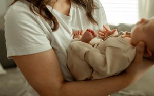 A close-up view of a person gently holding and cradling a small baby's feet in their hands.