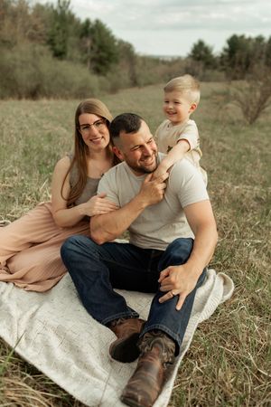 A young family sitting together on a blanket in a grassy field during golden hour.