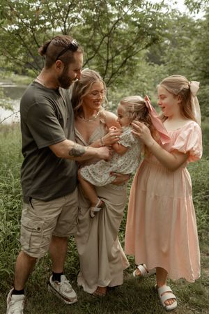 A family in casual attire stands together outdoors in a natural setting on a warm summer day.