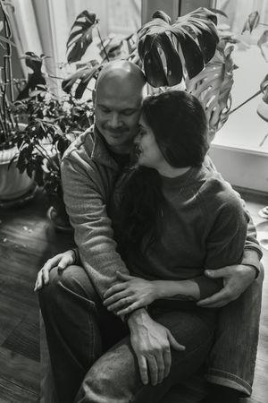 A couple shares an intimate moment while sitting together on a dark couch in a black and white photograph.