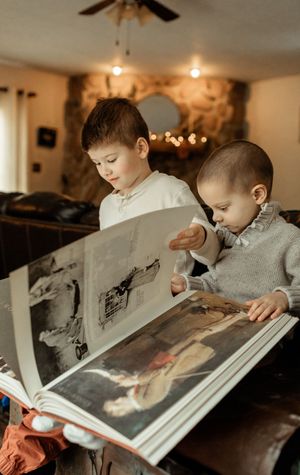Two children lean over a large book together while reading in warm indoor lighting.