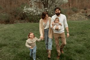 A family wearing coordinated earth-toned outfits runs and plays together in a grassy outdoor setting at sunset.