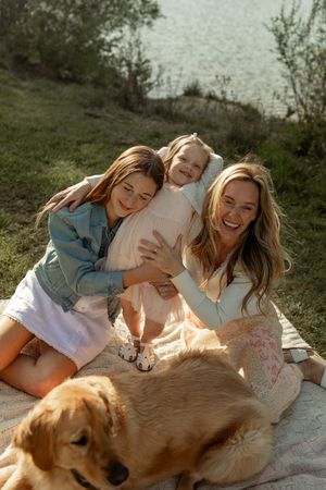 A group sits together on a blanket outdoors with a friendly golden retriever on a sunny afternoon.