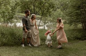 People in light flowy dresses dance together in a whimsical woodland setting during golden hour.