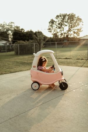 Pink toy car parked on concrete during golden hour sunset with trees in background.