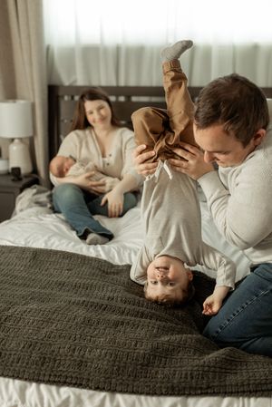 Family relaxing together on bed in casual clothing during intimate lifestyle photoshoot.