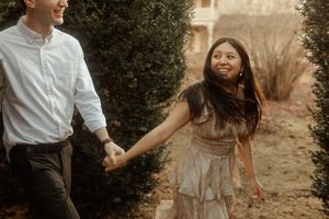 A joyful couple walks and dances together in a garden setting during an engagement photoshoot session at sunset.