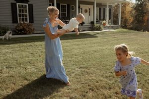 A child plays joyfully in a sunny backyard with a house visible in the background.