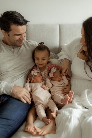 Family relaxing together on white couch with twin babies and toddler in matching outfits.