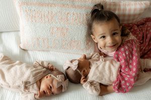 A series of connected photos showing a baby lying on white bedding wearing pink and beige outfits.