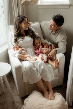 A family shares tender moments together on a white couch near a bright window in a series of intimate photographs.