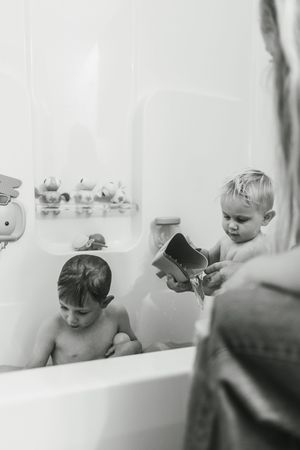 A series of black and white photos showing a baby enjoying bath time in a white bathtub.