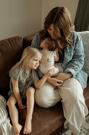Family sharing tender moments together on brown couch in soft natural light.
