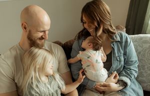Family sitting together on couch sharing tender moment with their baby in casual home setting.