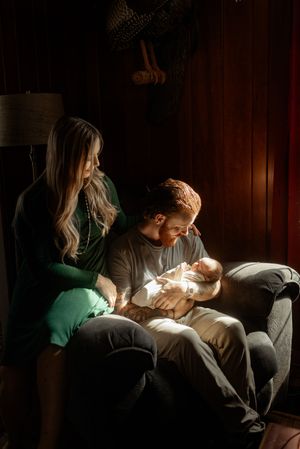 Parents tenderly care for their newborn baby in a series of intimate, dimly lit moments on a couch.