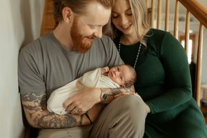 Parents lovingly cradle their newborn baby while sitting together on a couch at home.