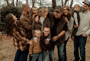 A large family group poses together outdoors on a fall day wearing casual clothing in earth tones.