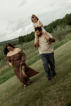 A playful couple enjoys a fun moment on a grassy hill during a casual outdoor photoshoot.