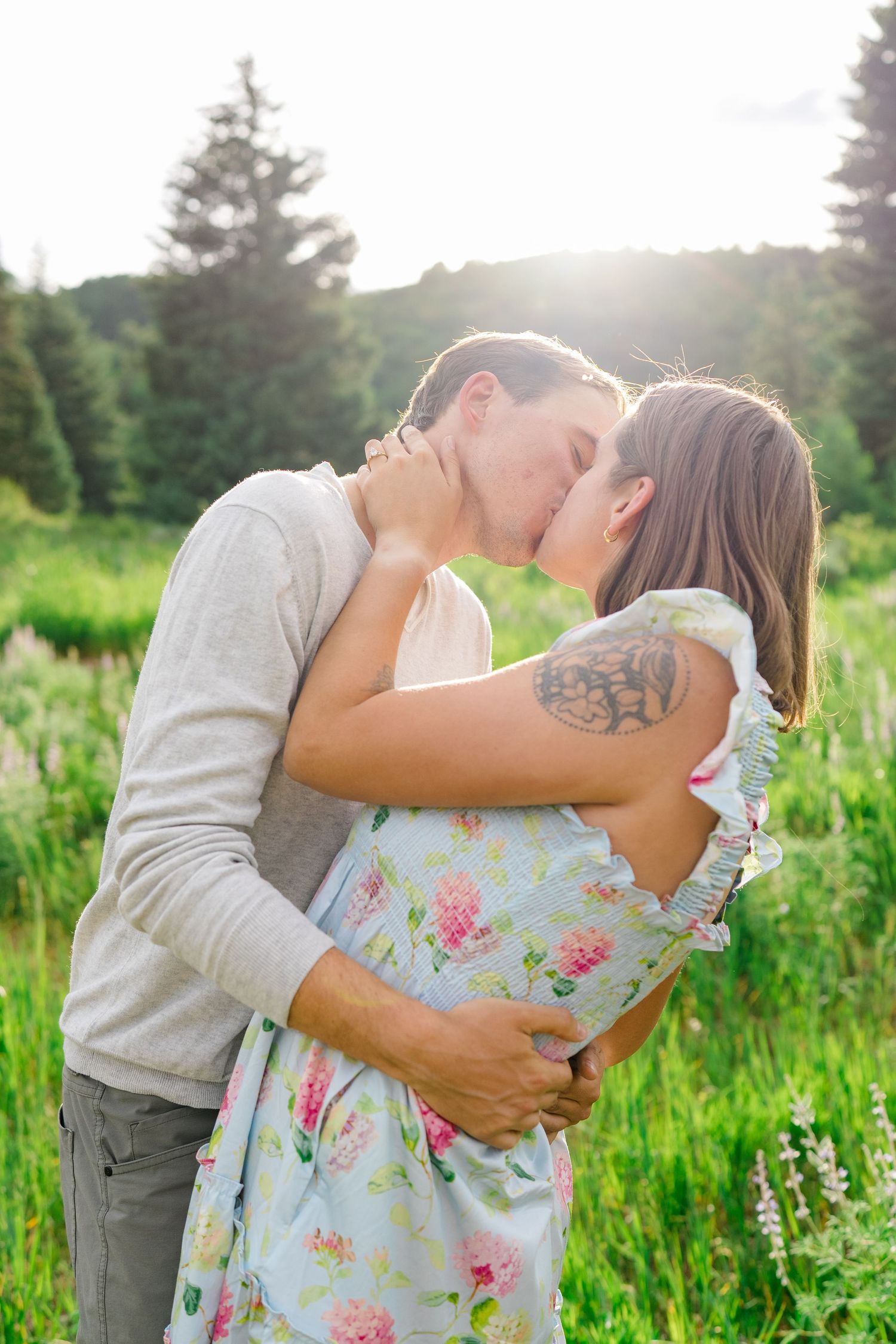 guy and girl kissing during engagement photo session, lush greenery behind them