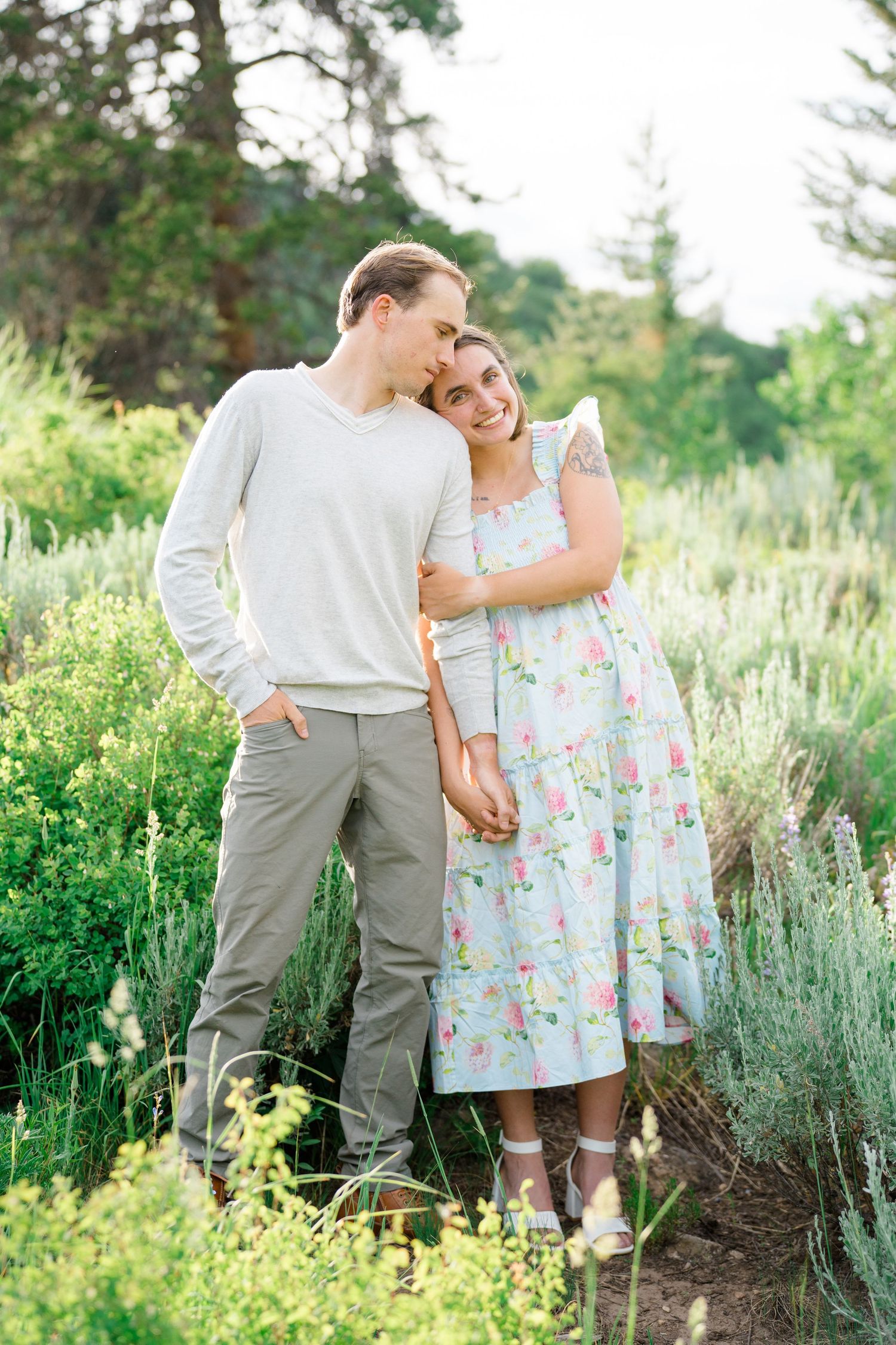 girl cozying up to guy during engagement session, lush greenery behind them